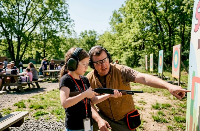 Child receiving supervised shooting instruction outdoors