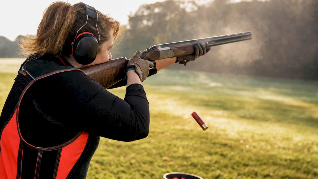 Female shooter managing recoil during clay shooting
