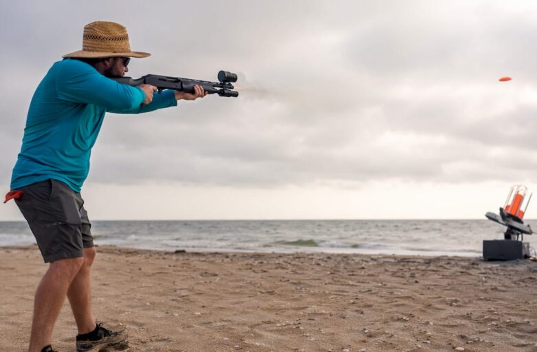 Man aiming modified shotgun at clay target outdoors
